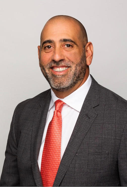 a headshot of a man wearing a suit and a red tie. 